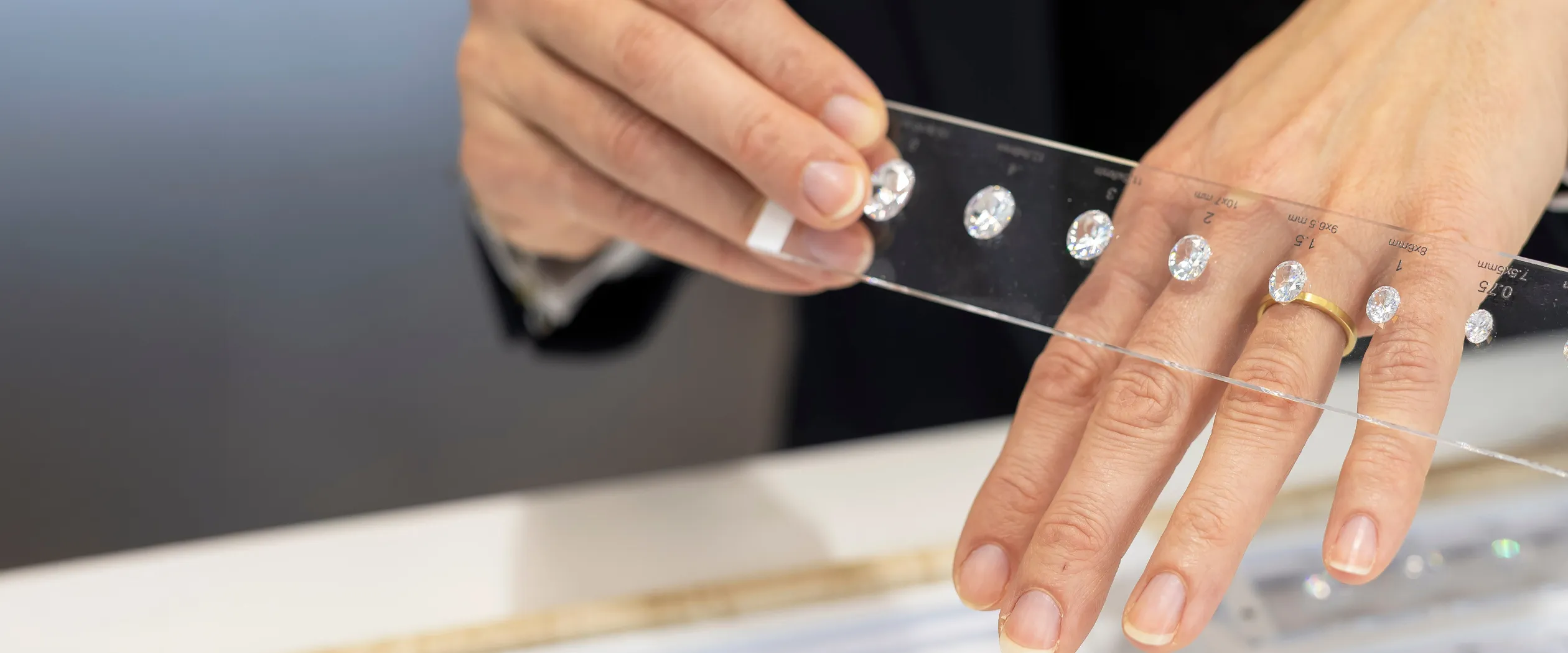Hands holding a strip with various diamond sizes for comparison.