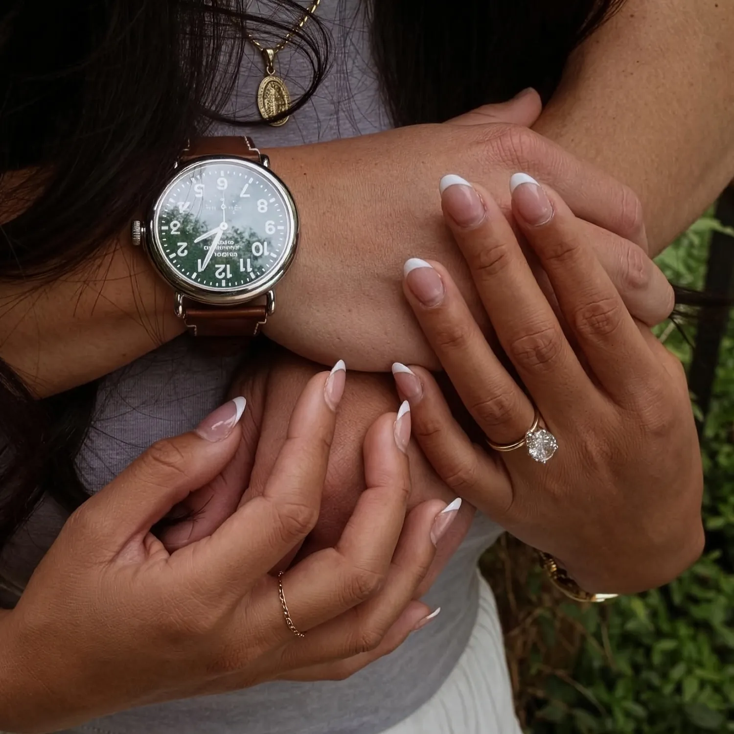 Two hands with French manicures, one wearing a watch, the other with a diamond ring.
