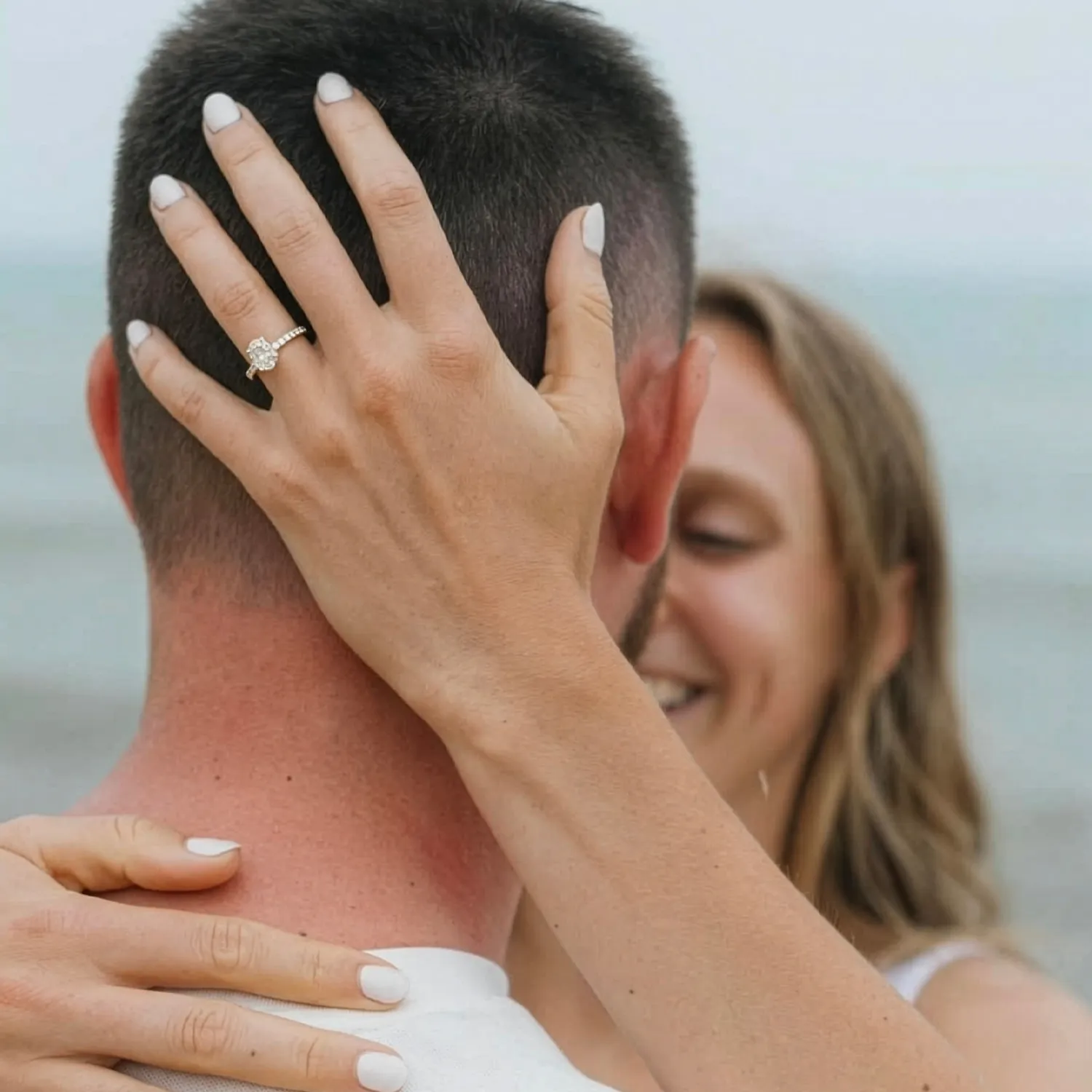 A woman embraces a man, showcasing an engagement ring on her hand.