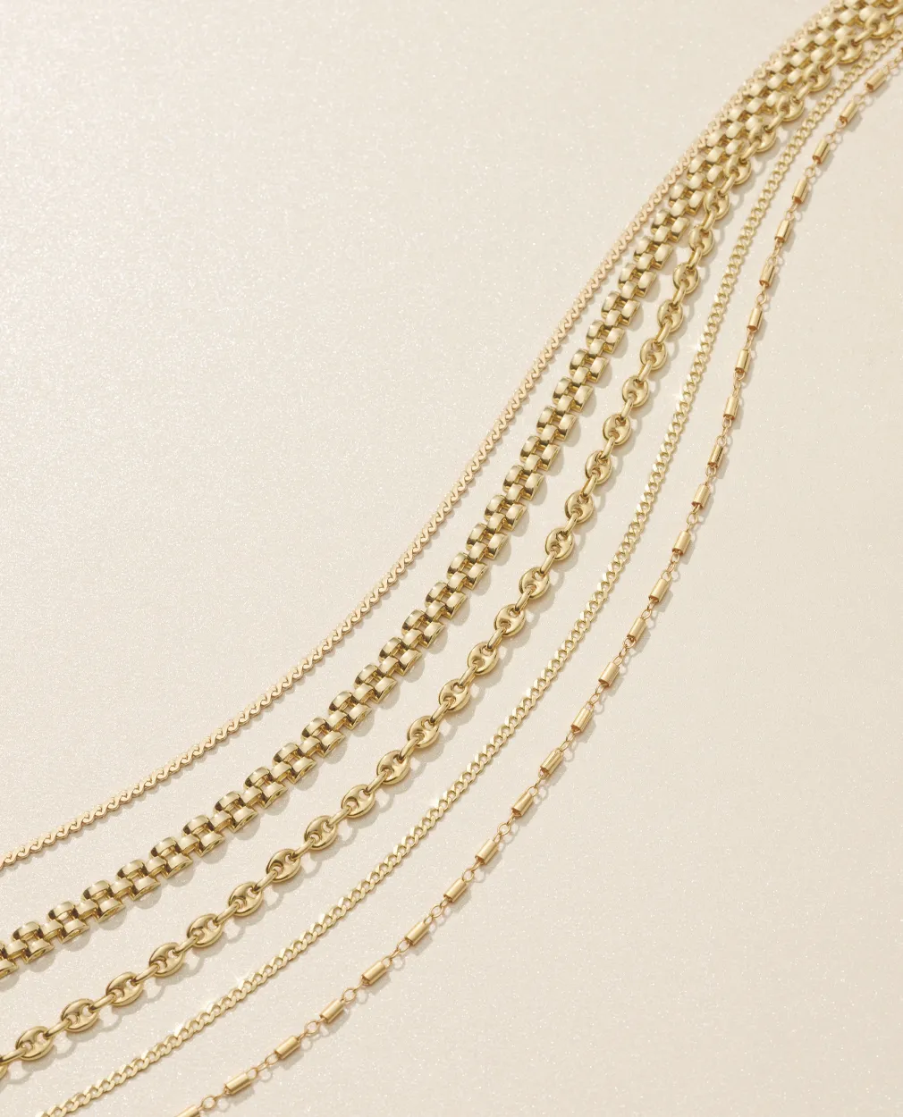 Gold chains of varying styles and thicknesses on a light background.