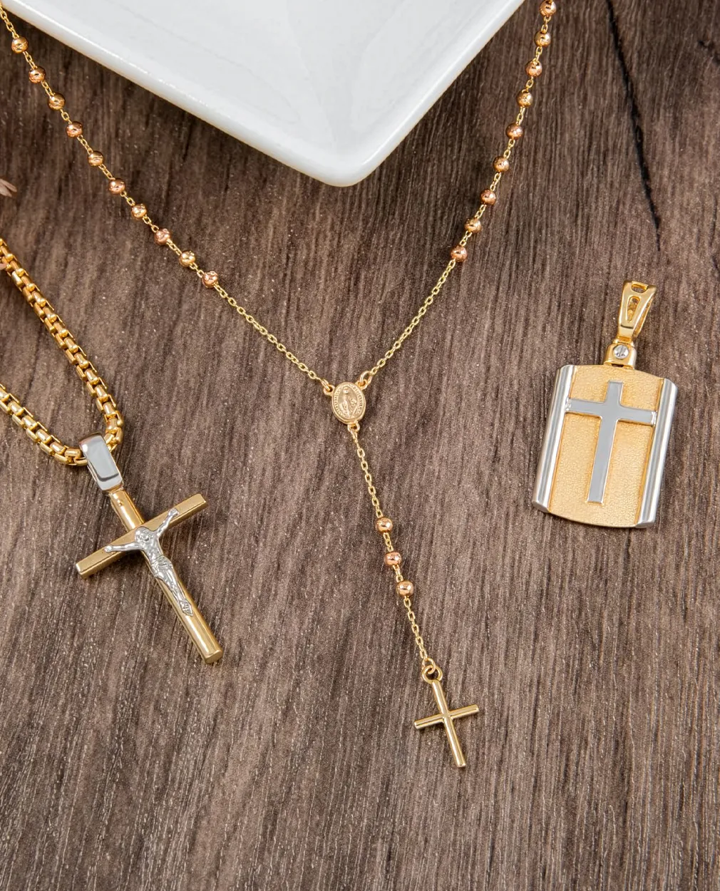 Gold and silver cross necklaces and pendant on wooden surface.