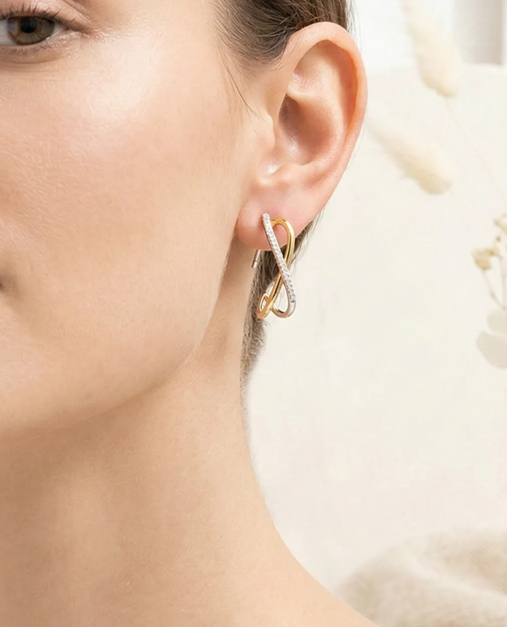 Gold and silver infinity loop earrings on a woman's ear.