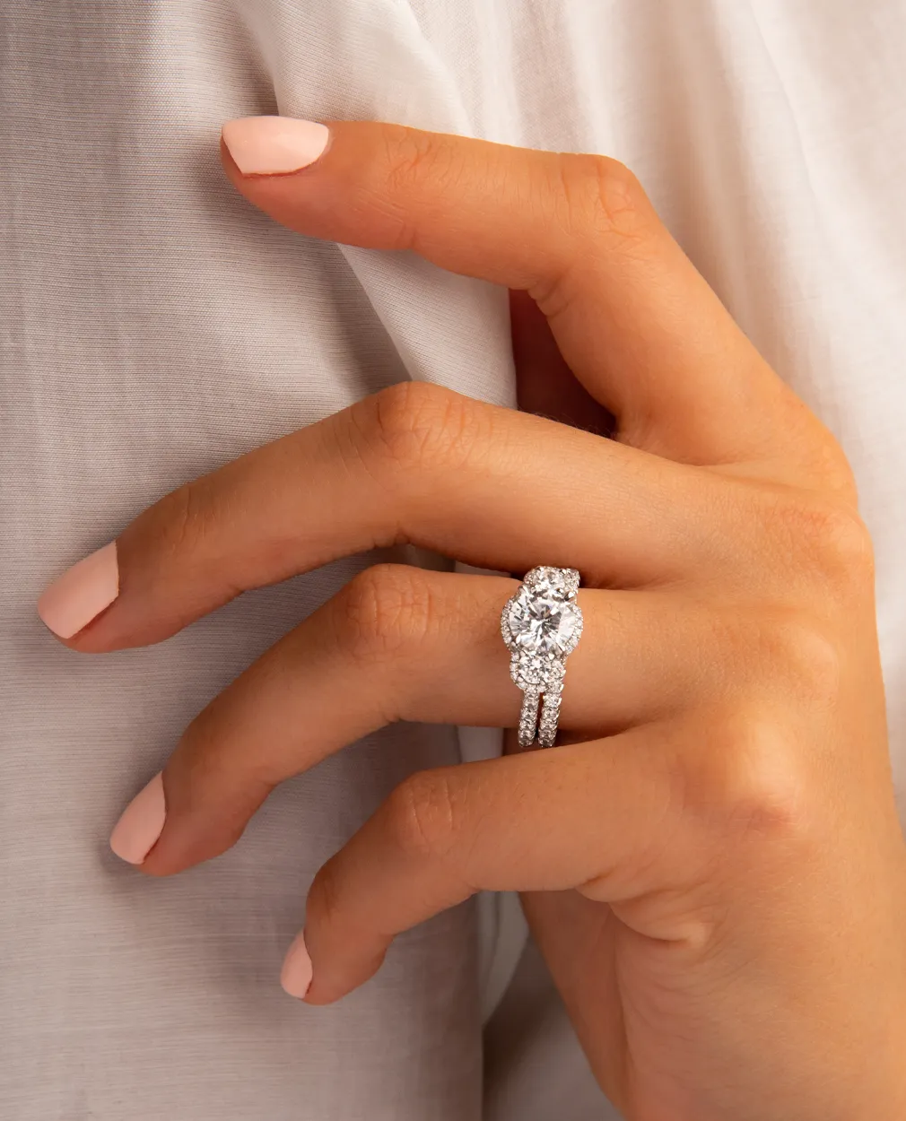 Hand with light pink nails wearing a sparkling diamond engagement ring.
