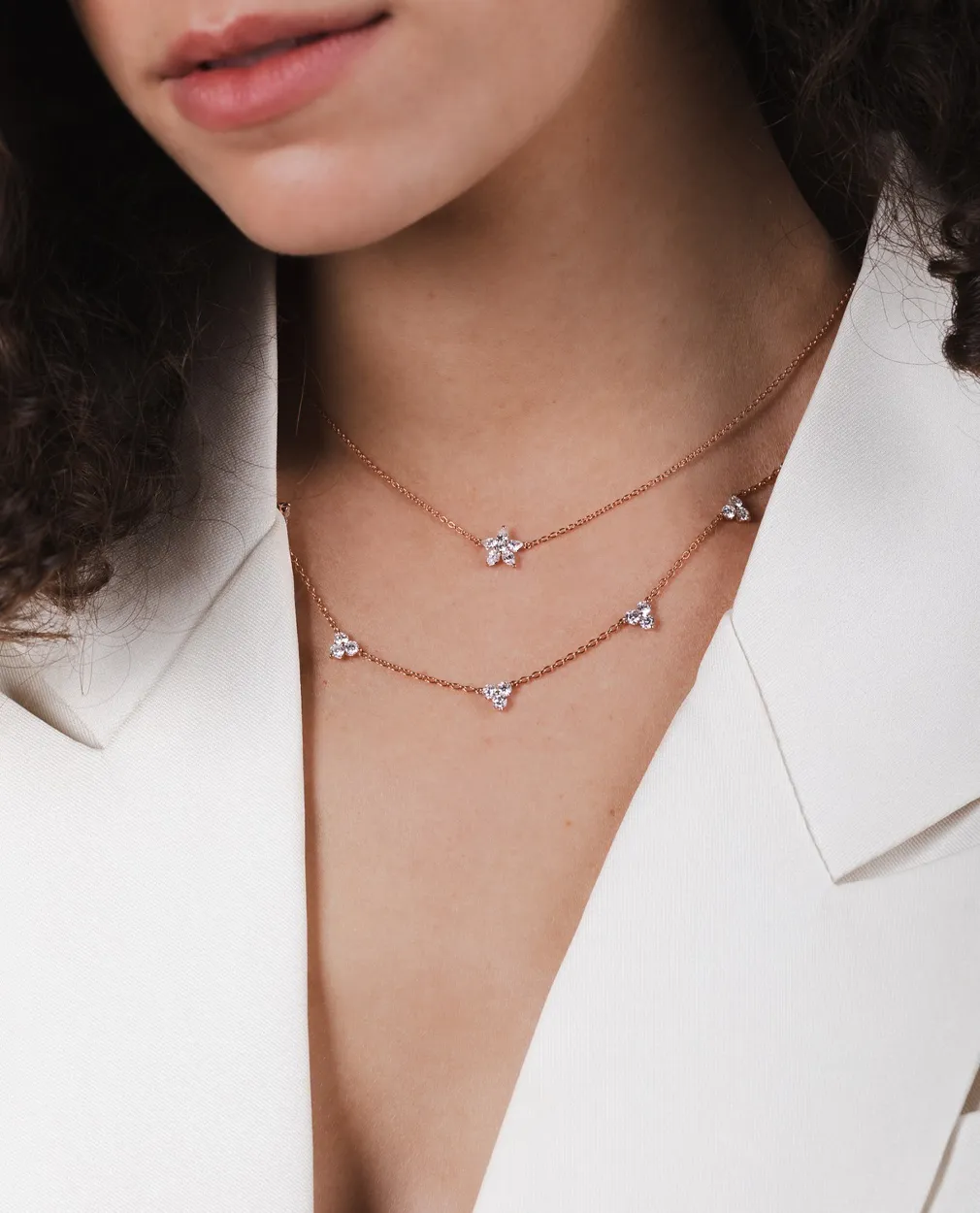 Woman wearing layered rose gold necklaces with diamond accents.