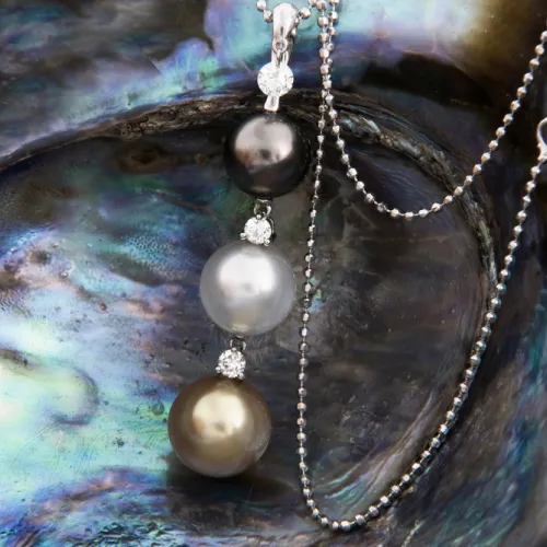 Elegant drop pendant necklace featuring black, silver, and golden pearls with diamond accents resting on an iridescent abalone shell.