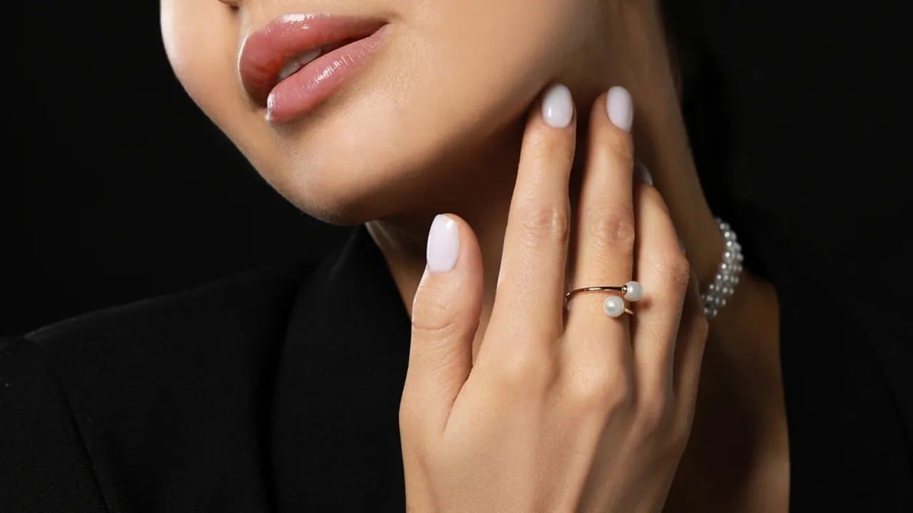 Close-up of a model wearing a modern open-wrap gold fashion ring featuring two white pearls.
