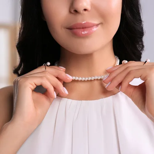 Lifestyle shot of a smiling woman adjusting a classic single-strand white pearl necklace around her neck.