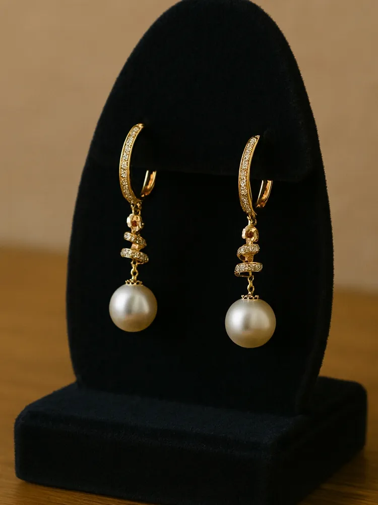 Elegant gold earrings with pearl drops and sparkling accents displayed on a black stand.
