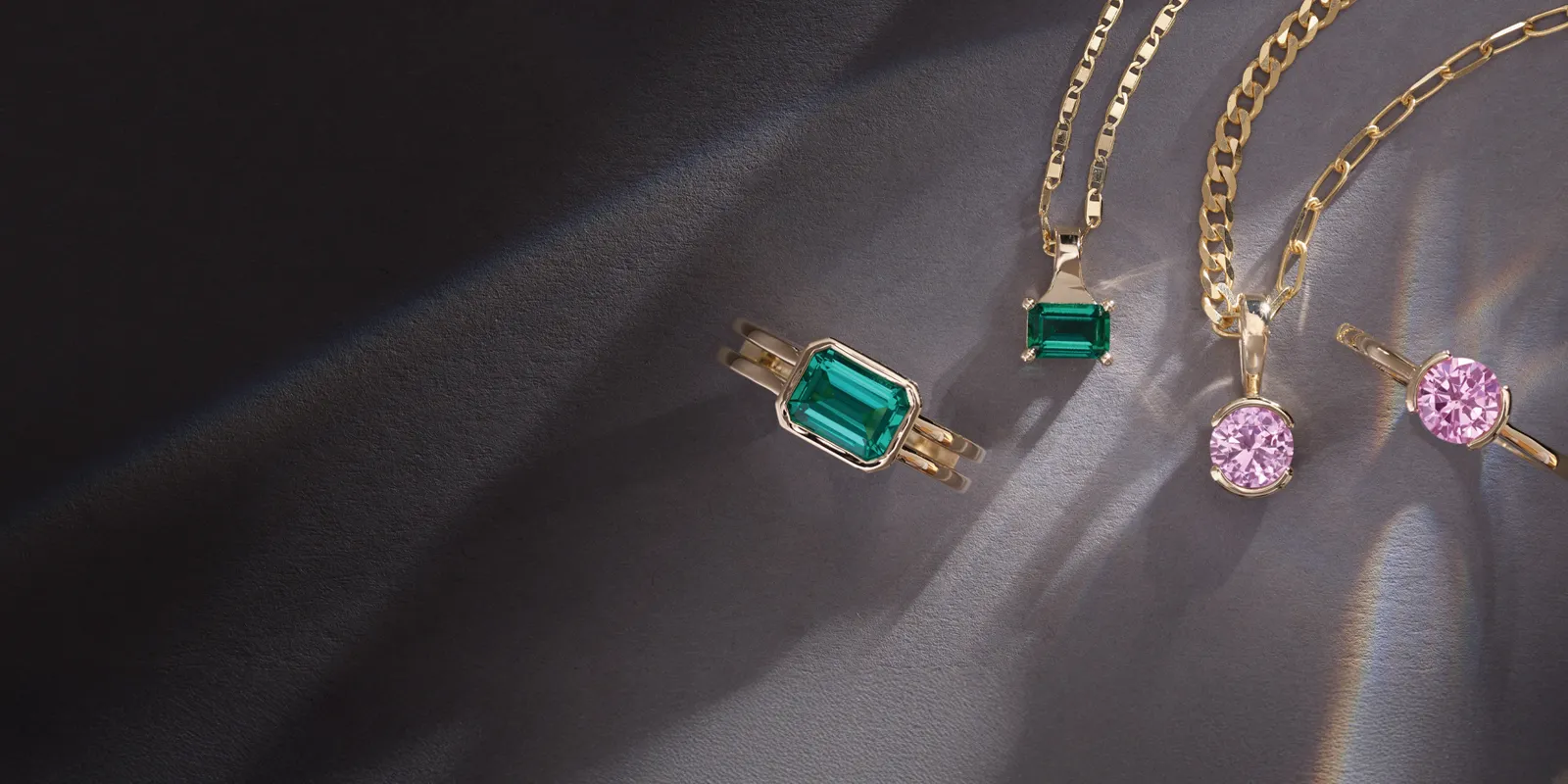 Elegant gold jewelry featuring emerald and pink gemstones, showcasing rings and necklaces.