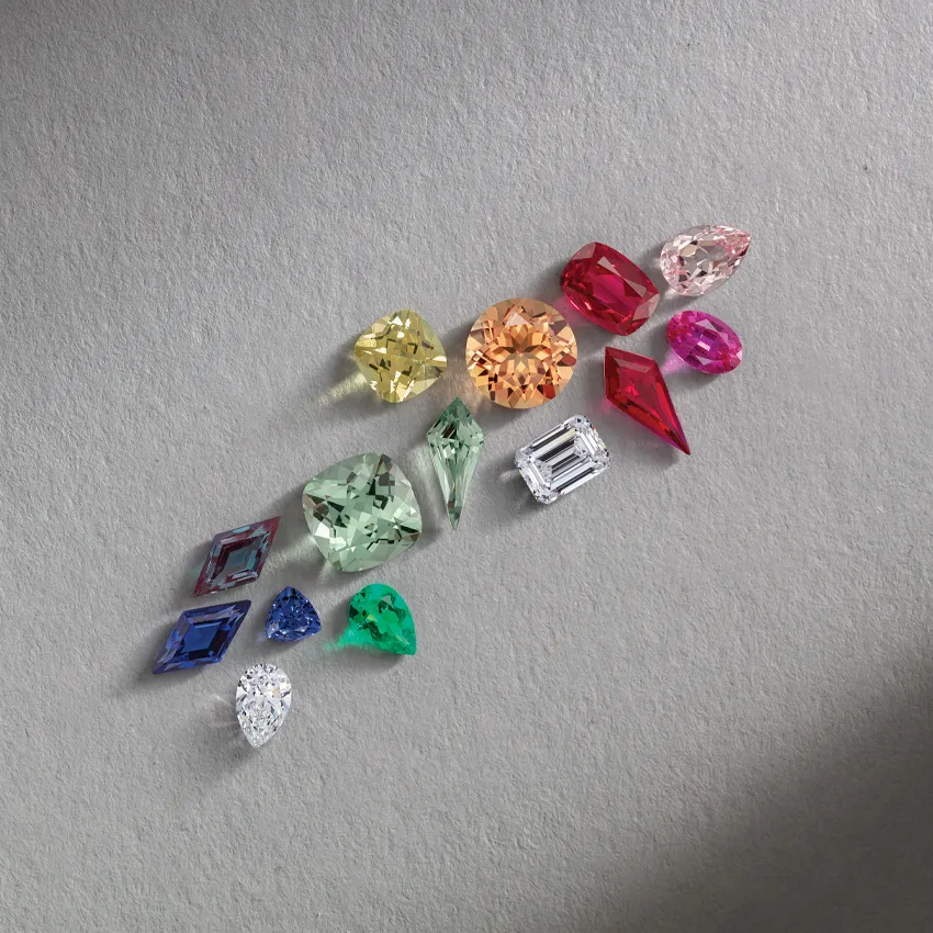 Colorful assortment of gemstones including diamonds, sapphires, and emeralds on a gray background.