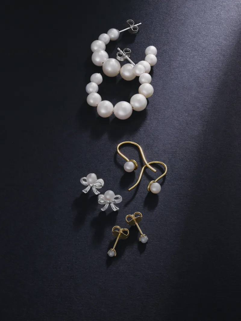 Elegant pearl jewelry set featuring earrings and a bracelet on a dark background.