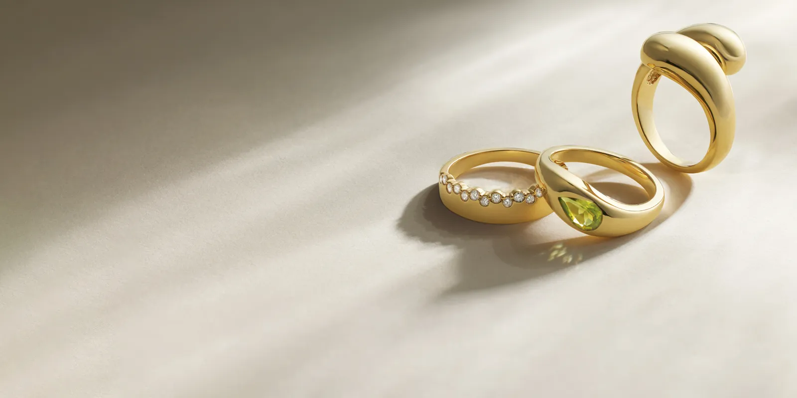 Three elegant gold rings featuring diamonds and a green gemstone, displayed on a soft surface.