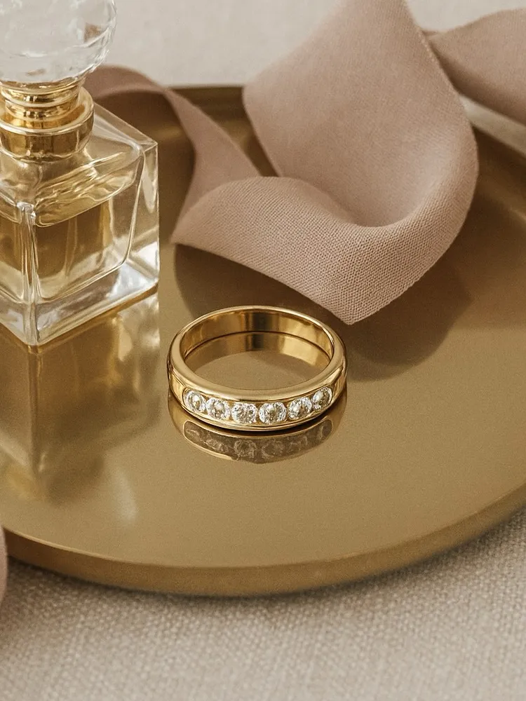 Gold ring with sparkling stones beside a perfume bottle on a golden tray, showcasing elegance and luxury.