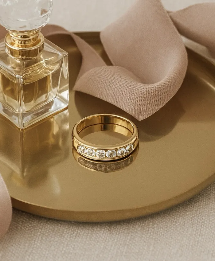 Gold ring with sparkling stones beside a perfume bottle on a golden tray, showcasing elegance and luxury.