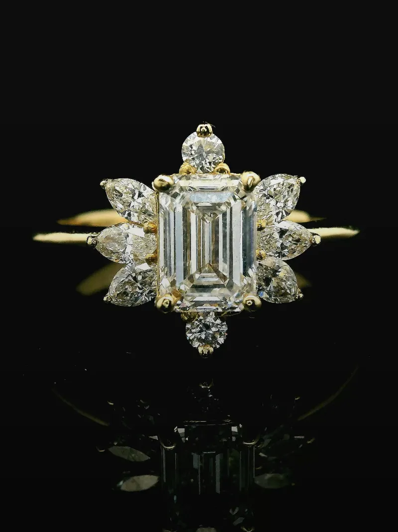 Elegant gold engagement ring featuring an emerald-cut diamond surrounded by smaller diamonds, set against a black background.