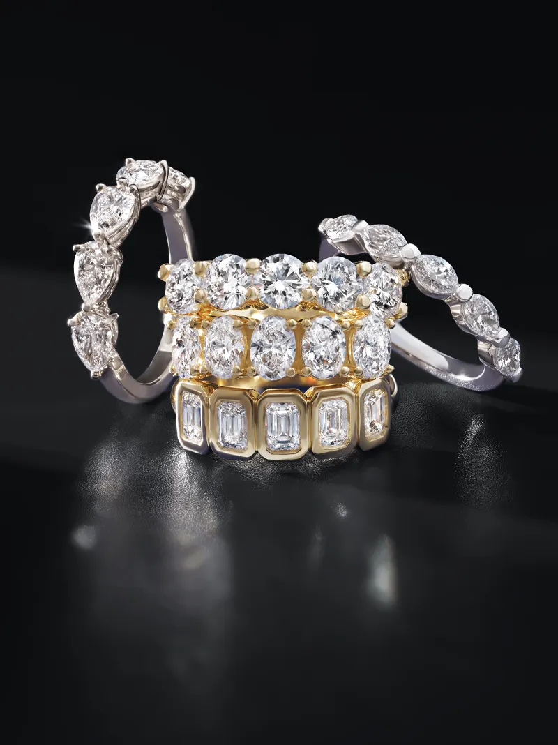 Four elegant diamond rings in gold and silver displayed on a dark background.