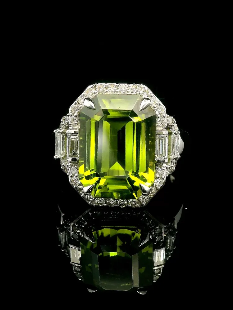 Stunning green gemstone ring with diamond accents, reflecting beautifully on a black surface.