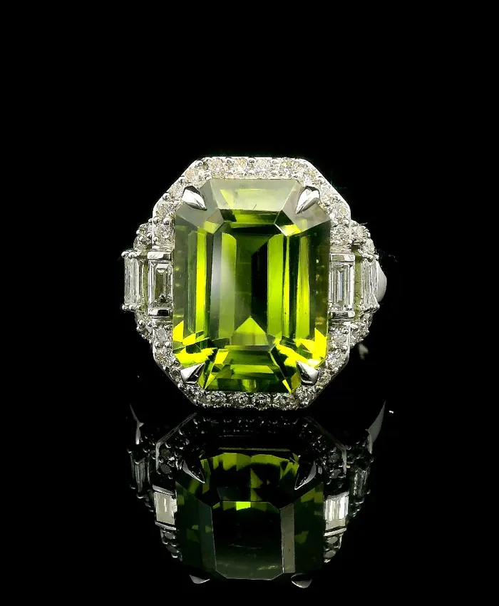 Stunning green gemstone ring with diamond accents, reflecting beautifully on a black surface.