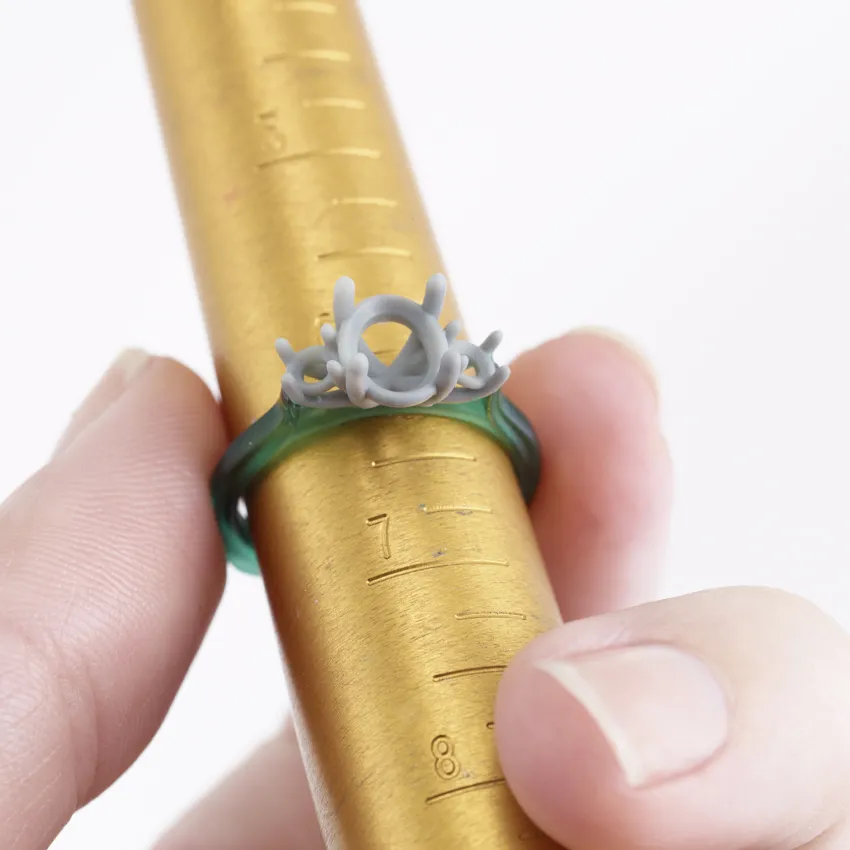 A hand holding a unique gray and green ring on a gold ring sizer, showcasing its intricate design.