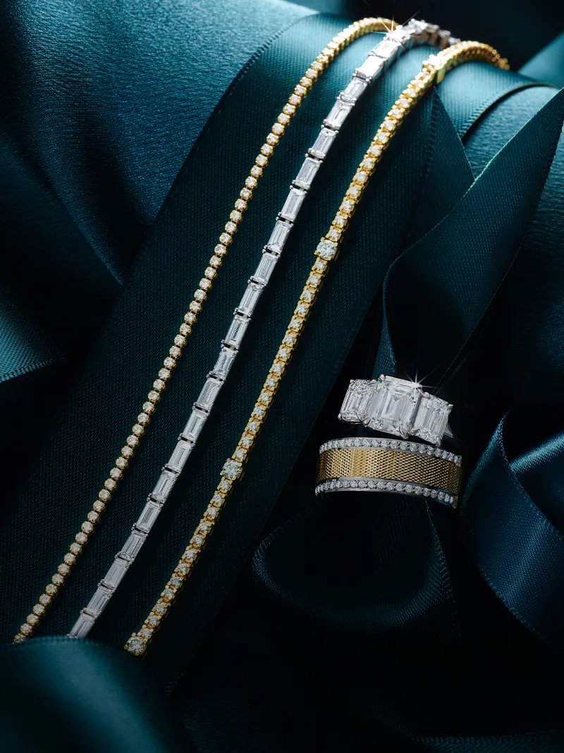Elegant diamond bracelets and rings displayed on dark teal fabric, showcasing luxury jewelry.