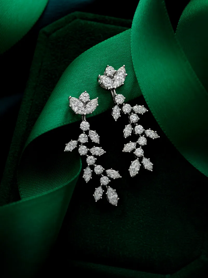 Elegant diamond earrings displayed on green ribbon, showcasing intricate floral design.
