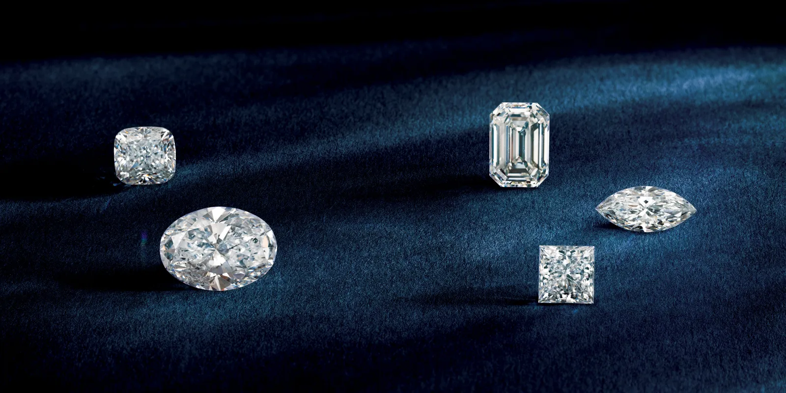 Five sparkling diamonds of various cuts displayed on a dark blue velvet background.
