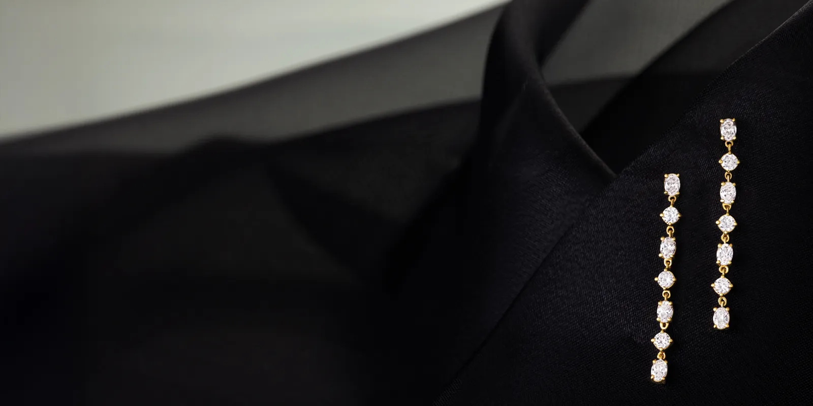 Elegant gold drop earrings with lab-grown diamonds, displayed on a black fabric background.
