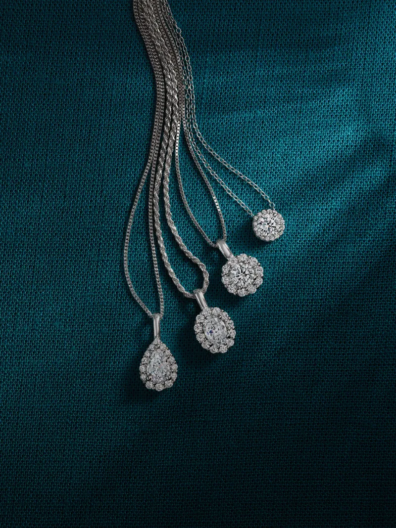 Four elegant diamond necklaces displayed on a teal fabric background.