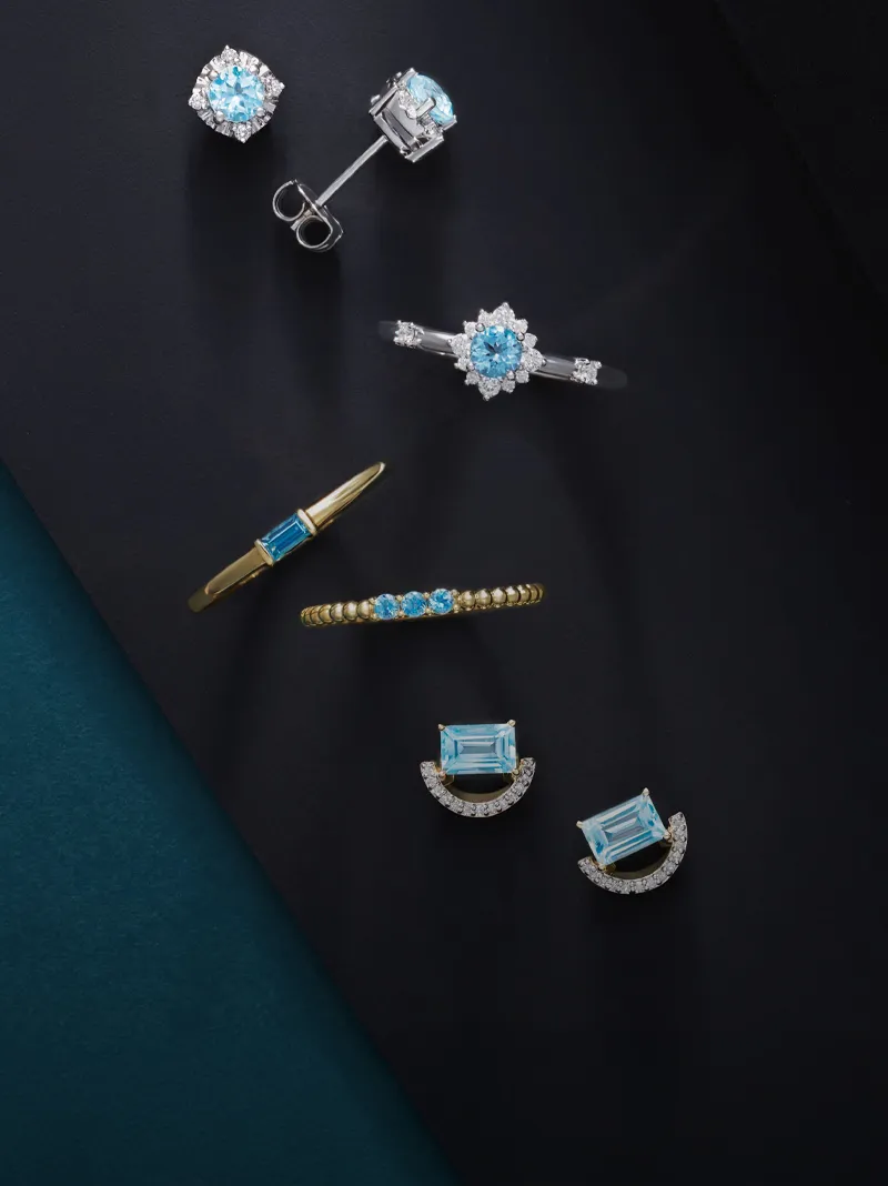 Aquamarine jewelry collection featuring rings, earrings, and a bracelet on a dark background.