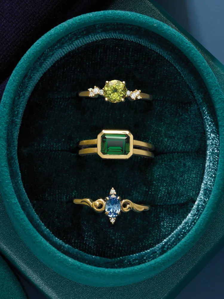 Three elegant gold rings featuring gemstones in a velvet jewelry box.