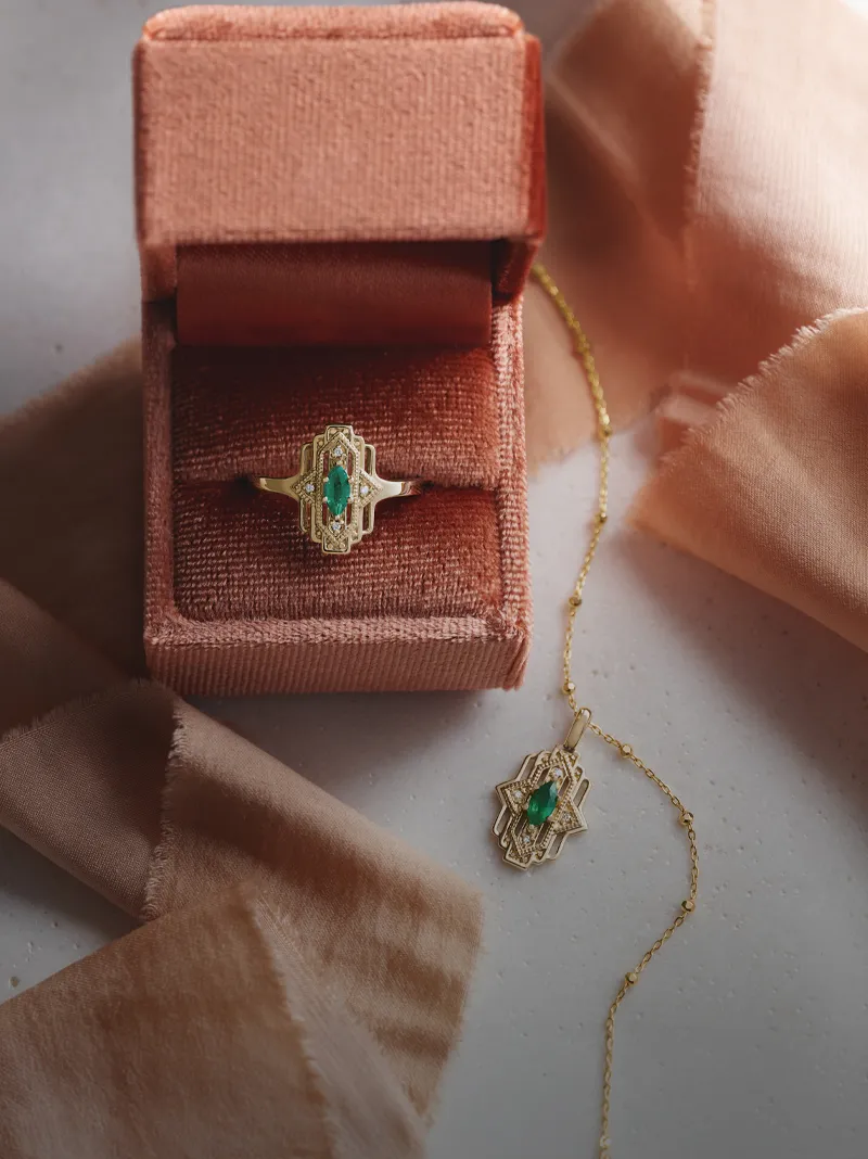 Emerald ring and pendant displayed in a velvet box with soft fabric.