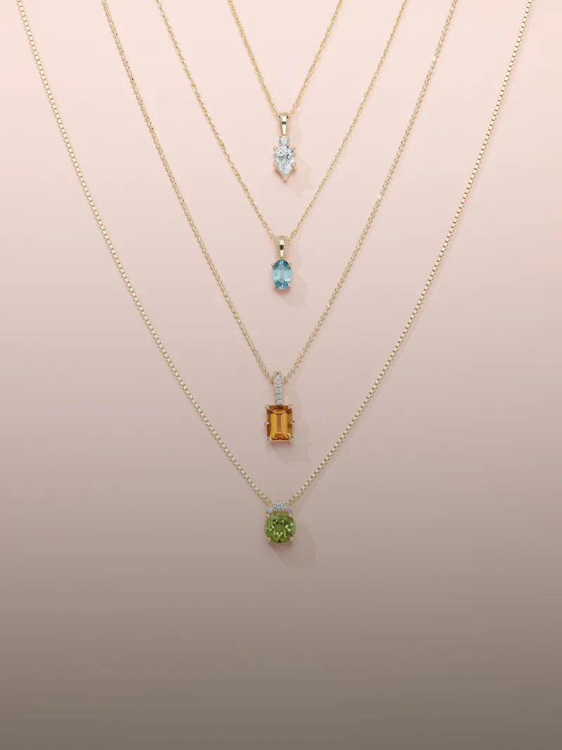 Layered gold necklaces with colorful gemstones displayed on a soft pink background.