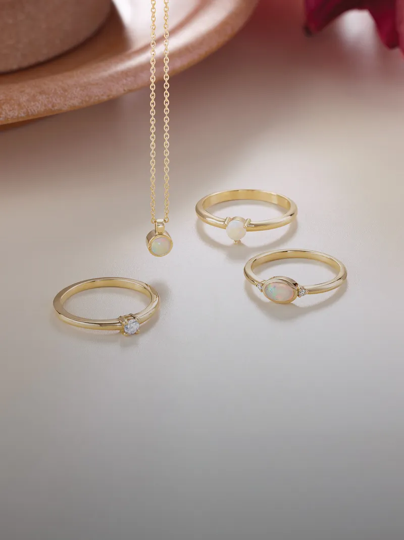 Three gold rings featuring opals and a diamond, alongside a matching opal pendant necklace.