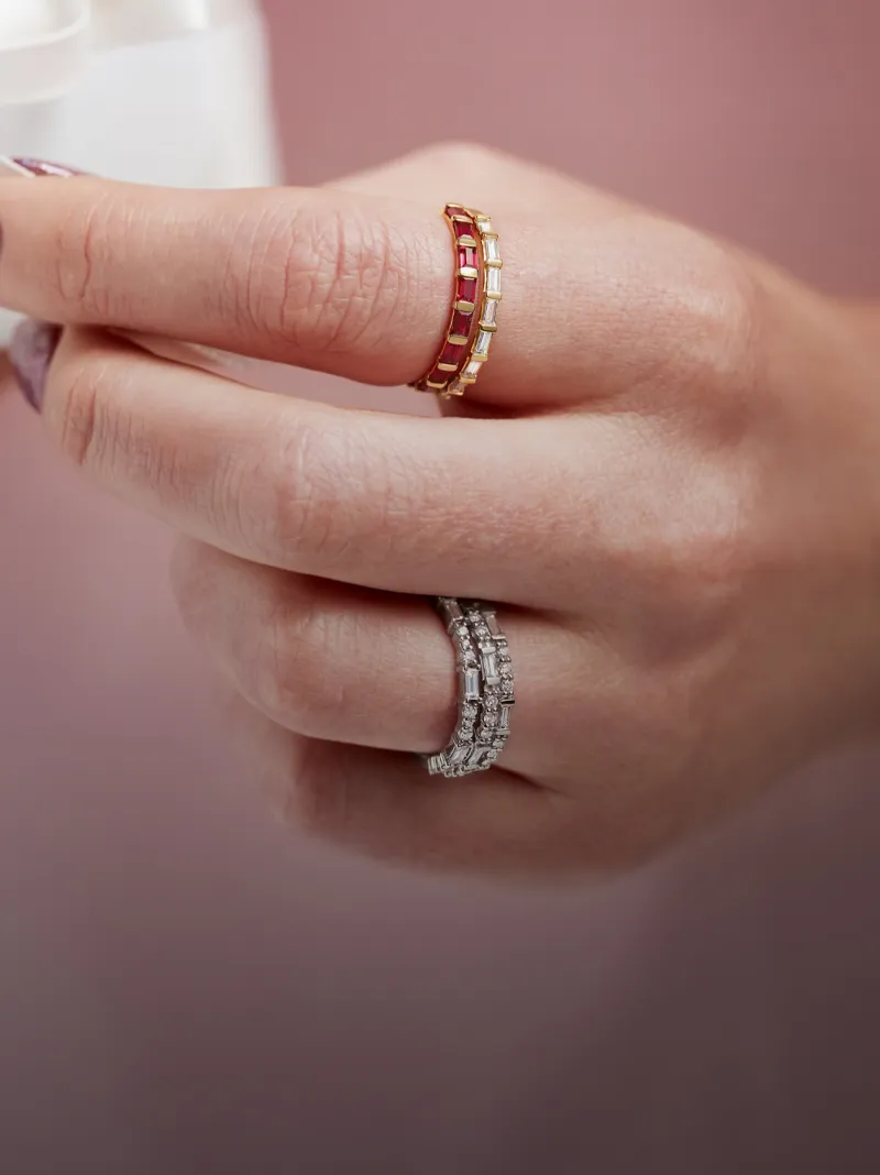 Two elegant rings, one with red stones and the other with clear stones, worn on a hand.
