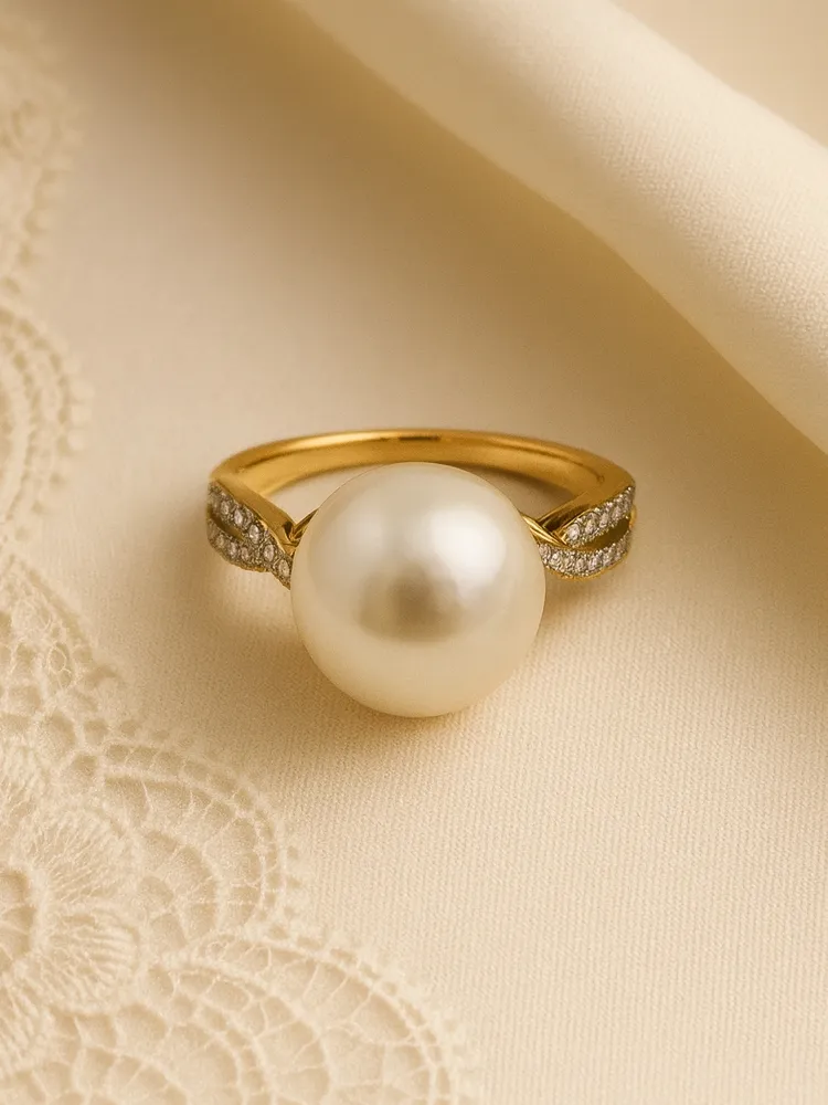 Elegant gold ring featuring a large pearl and diamond accents, displayed on a soft fabric background.