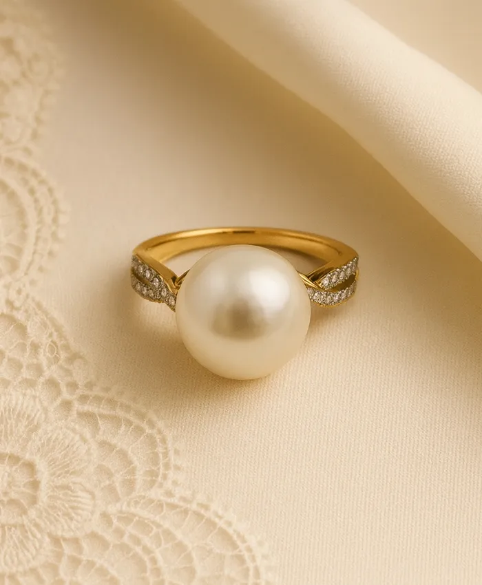 Elegant gold ring featuring a large pearl and diamond accents, displayed on a soft fabric background.