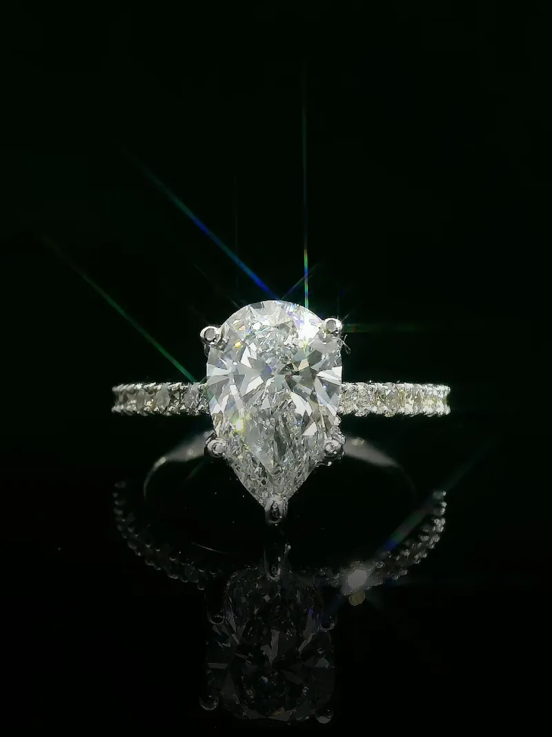 Stunning pear-shaped diamond engagement ring with sparkling accents, displayed against a dark background. Shop now at Geneva Jew