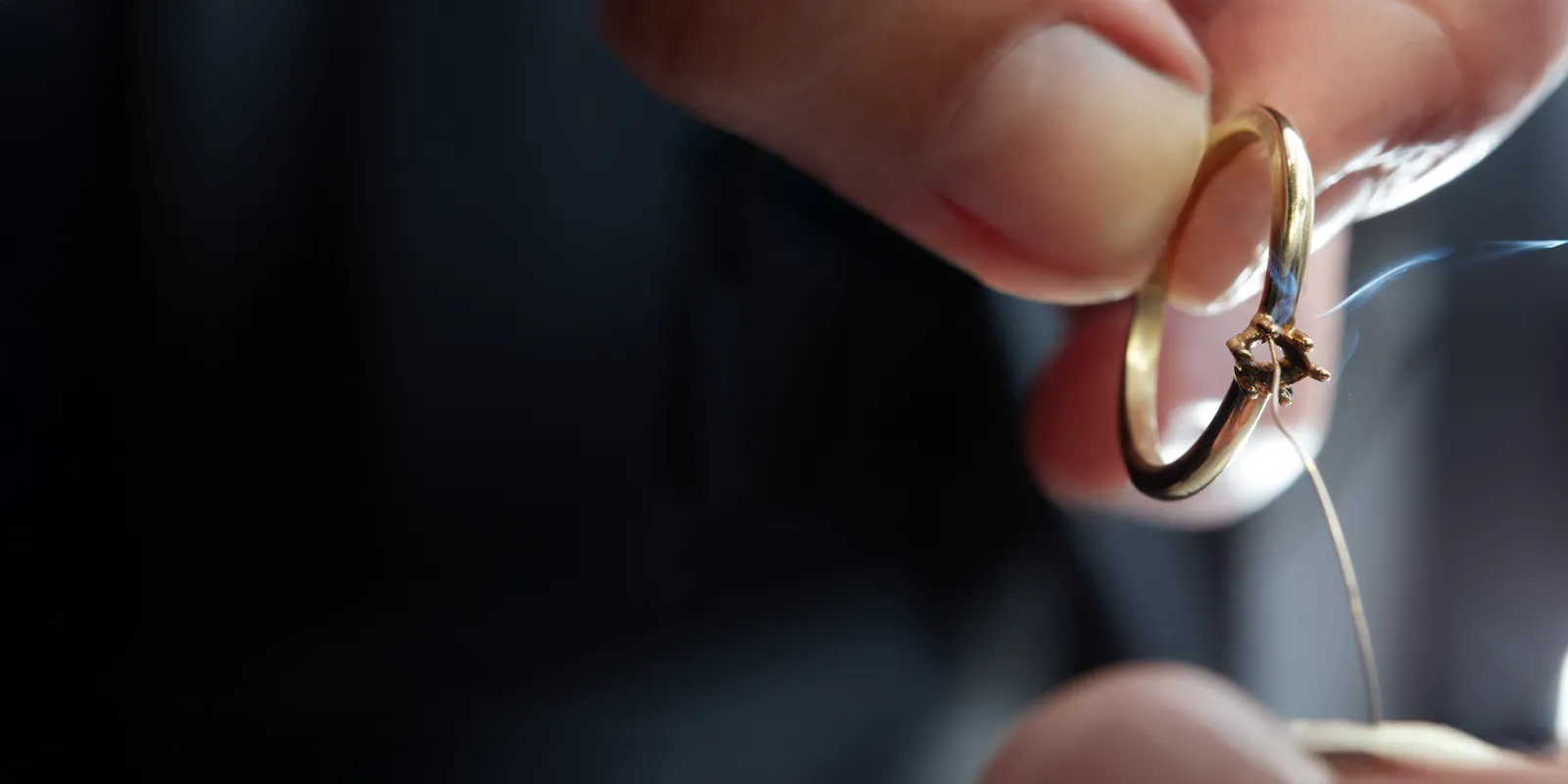 A jeweler holding a gold ring with a small flame, indicating repair work in progress. Click to view our services.
