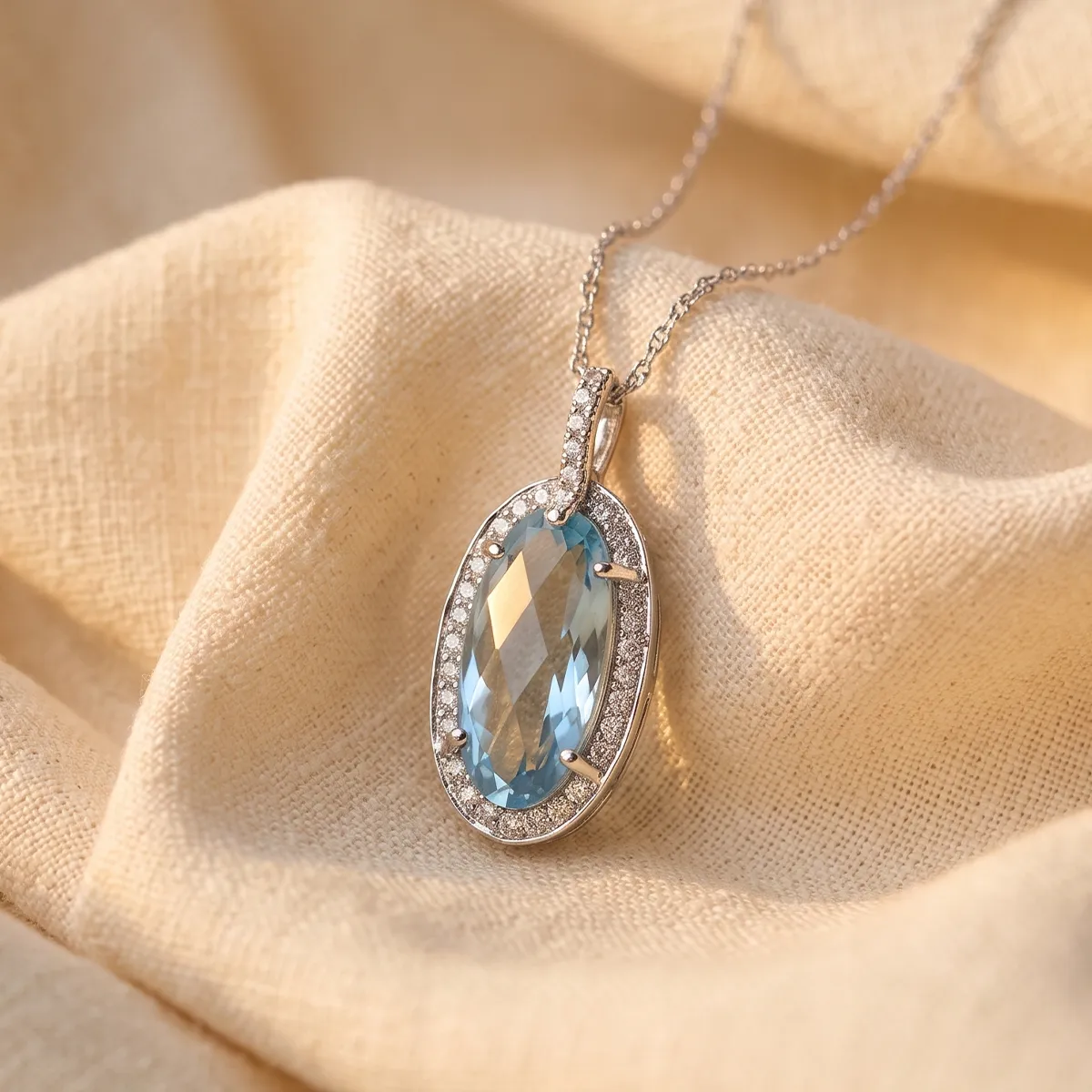A silver necklace with an oval blue gemstone pendant on a beige fabric background.