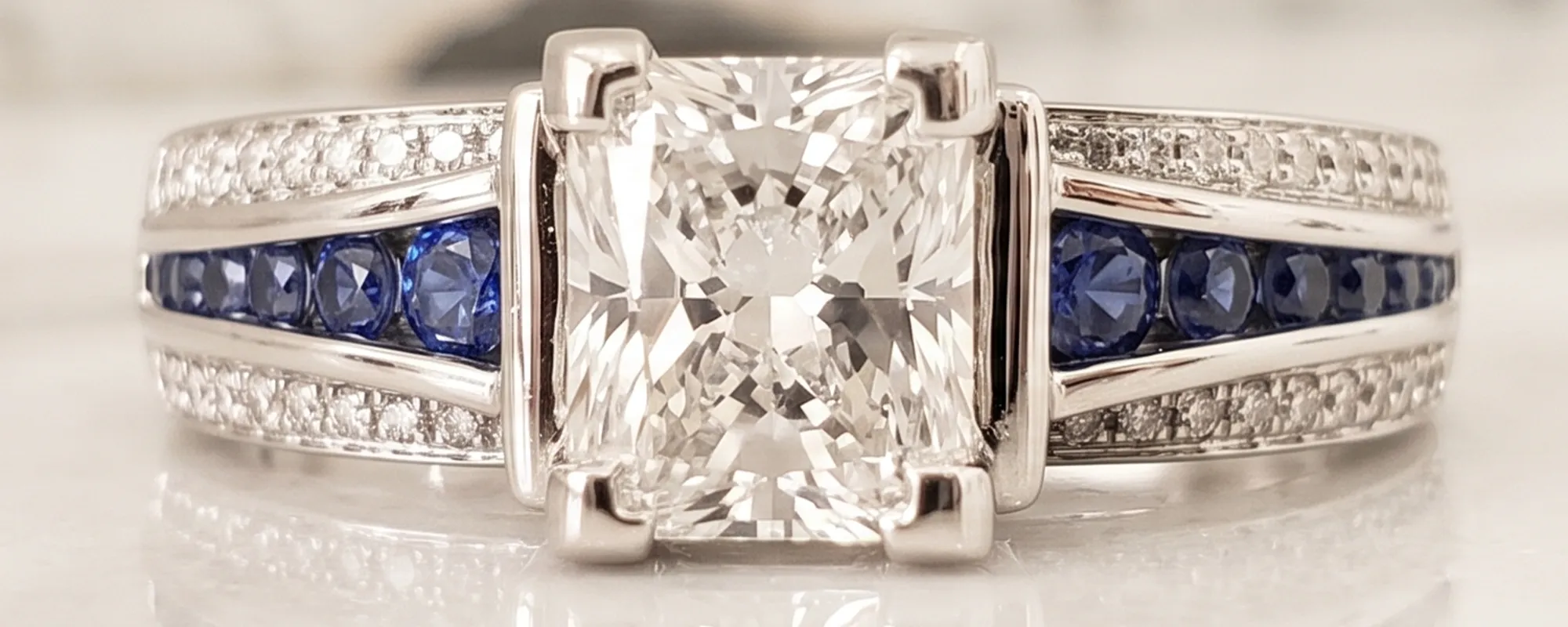 A diamond ring with blue and white gemstones set in a silver band on a marble surface.