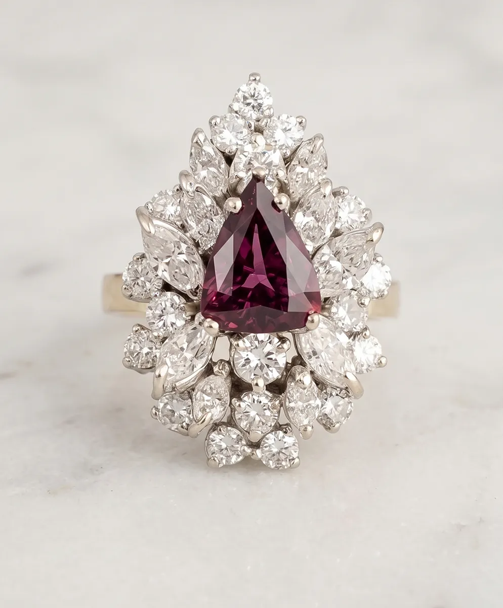A ring with a triangular red gemstone surrounded by sparkling diamonds on a marble surface.