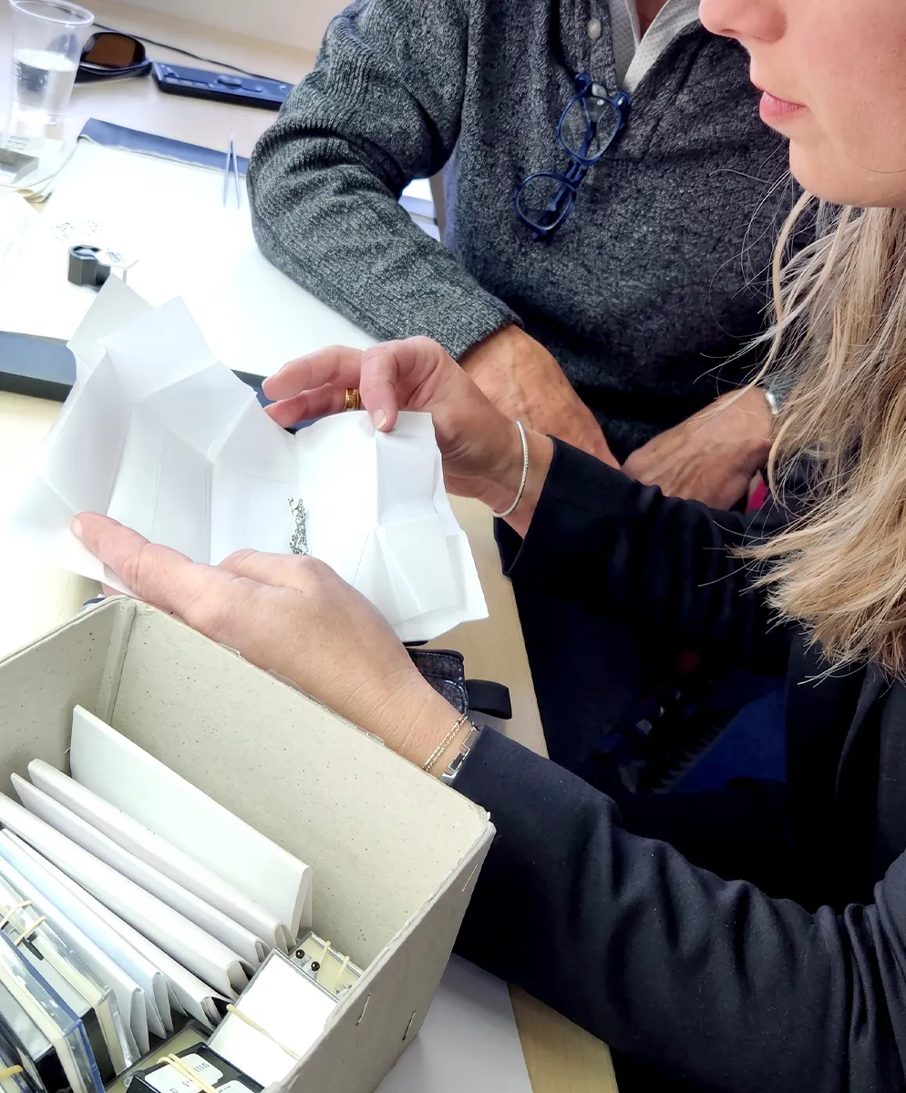 Two people examining jewelry on a table with a box of items nearby.