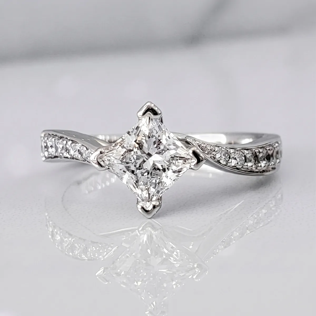 A princess-cut diamond ring with a twisted band on a reflective surface.
