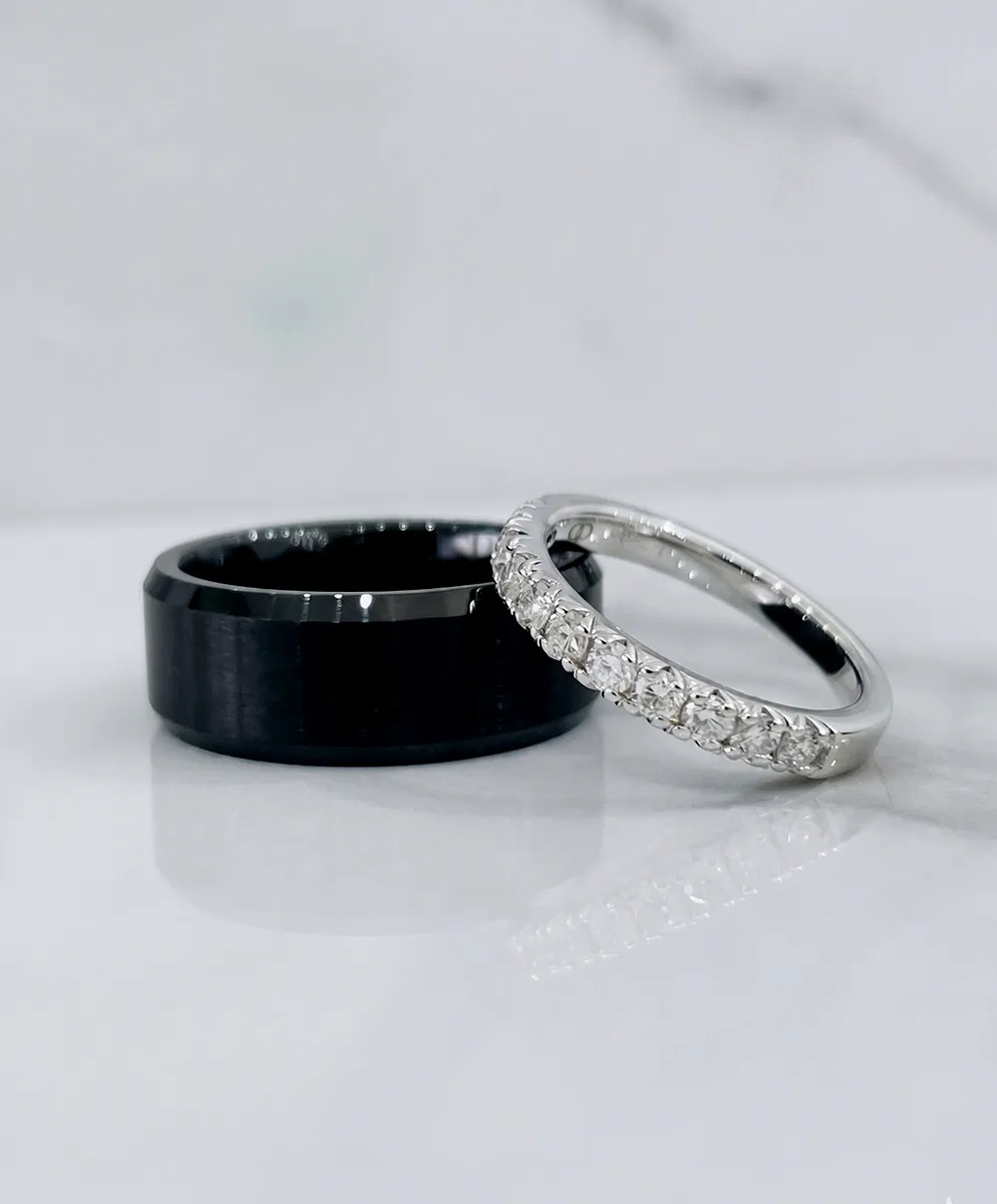 Two rings on a marble surface: a black band and a diamond-studded silver band.