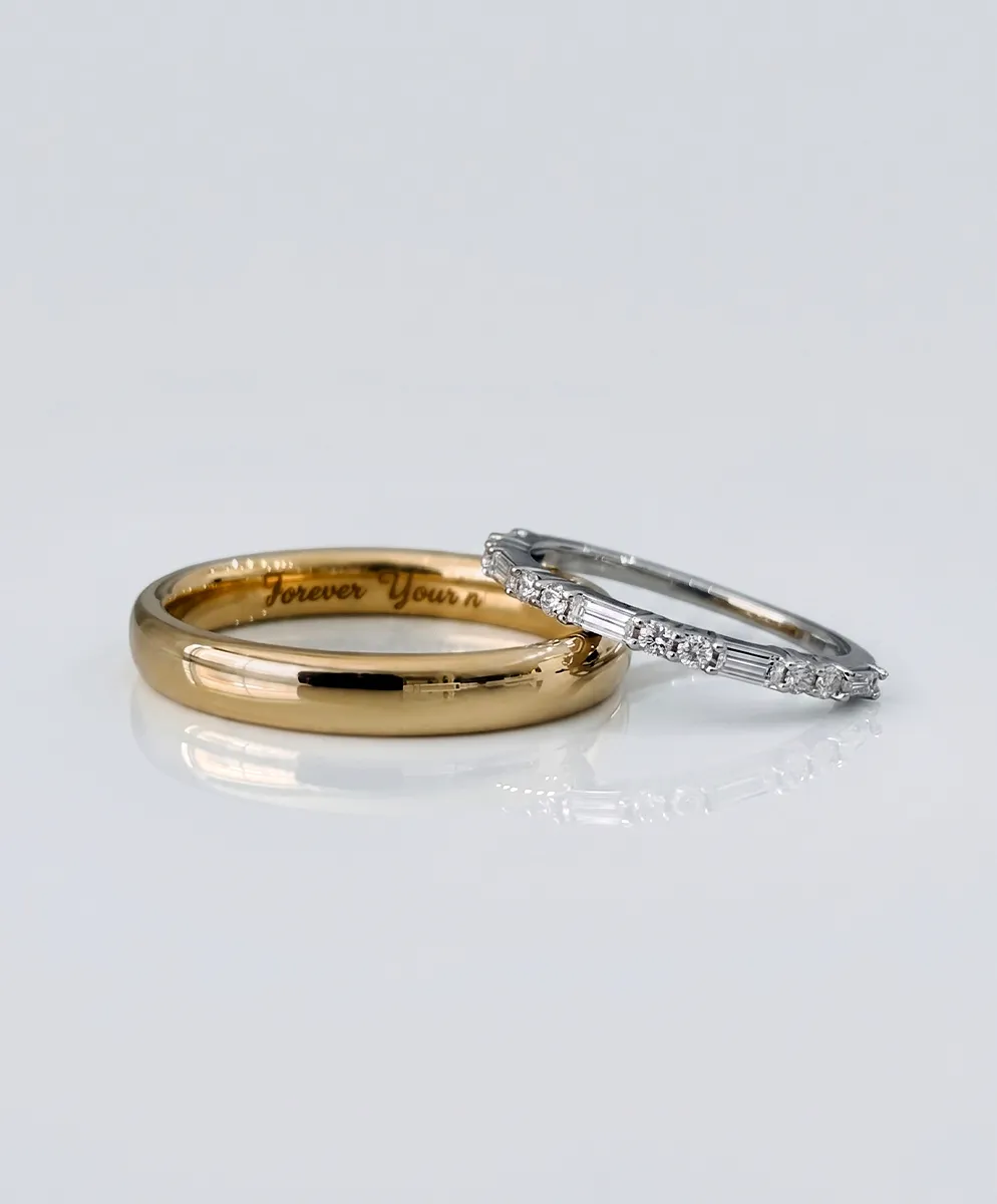 Two wedding bands: a gold band with engraving and a silver band with diamonds on a reflective surface.