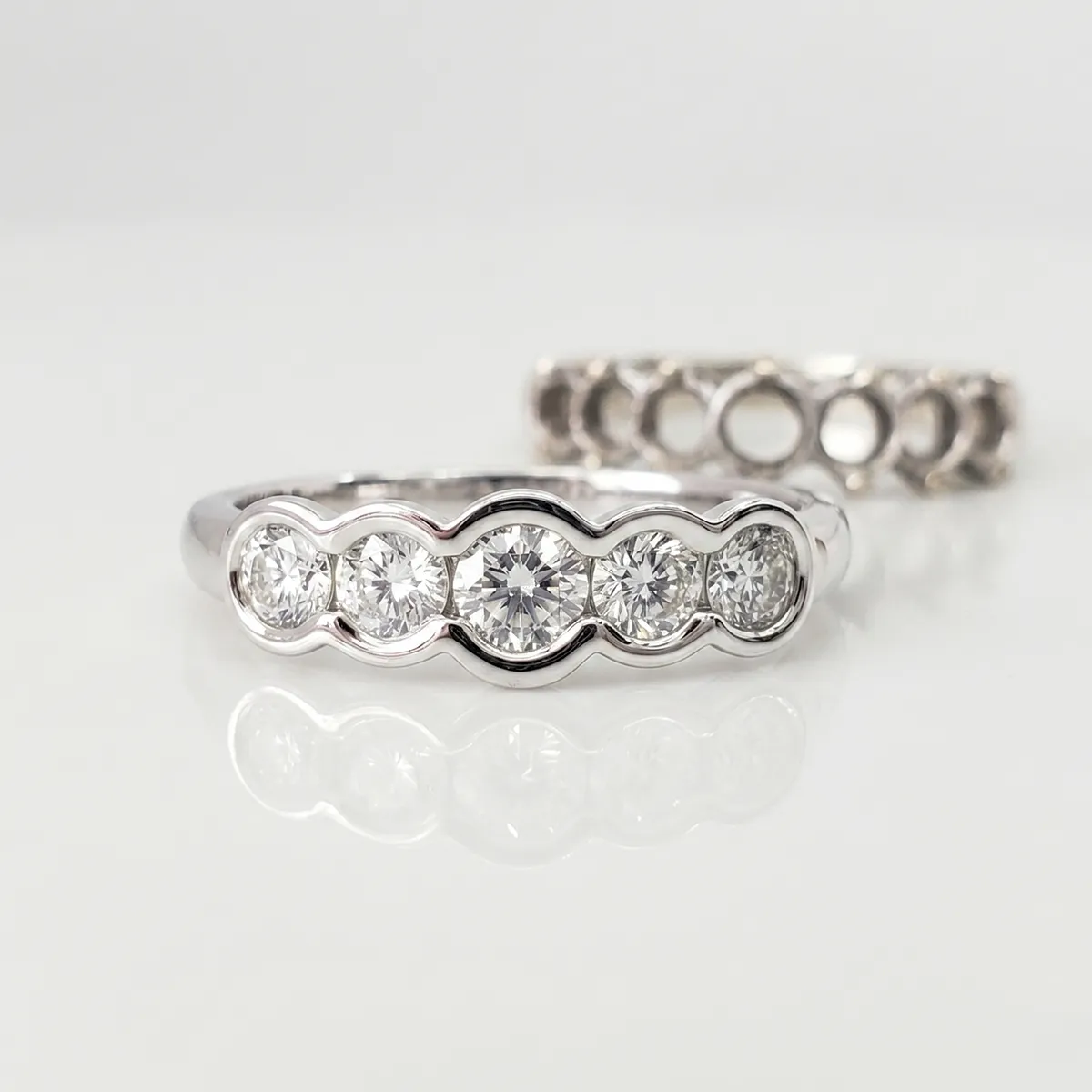 Diamond ring with five stones in a row, reflecting on a white surface. Build a Women's Band at Georgetown Jewelers, Wood Dale, I