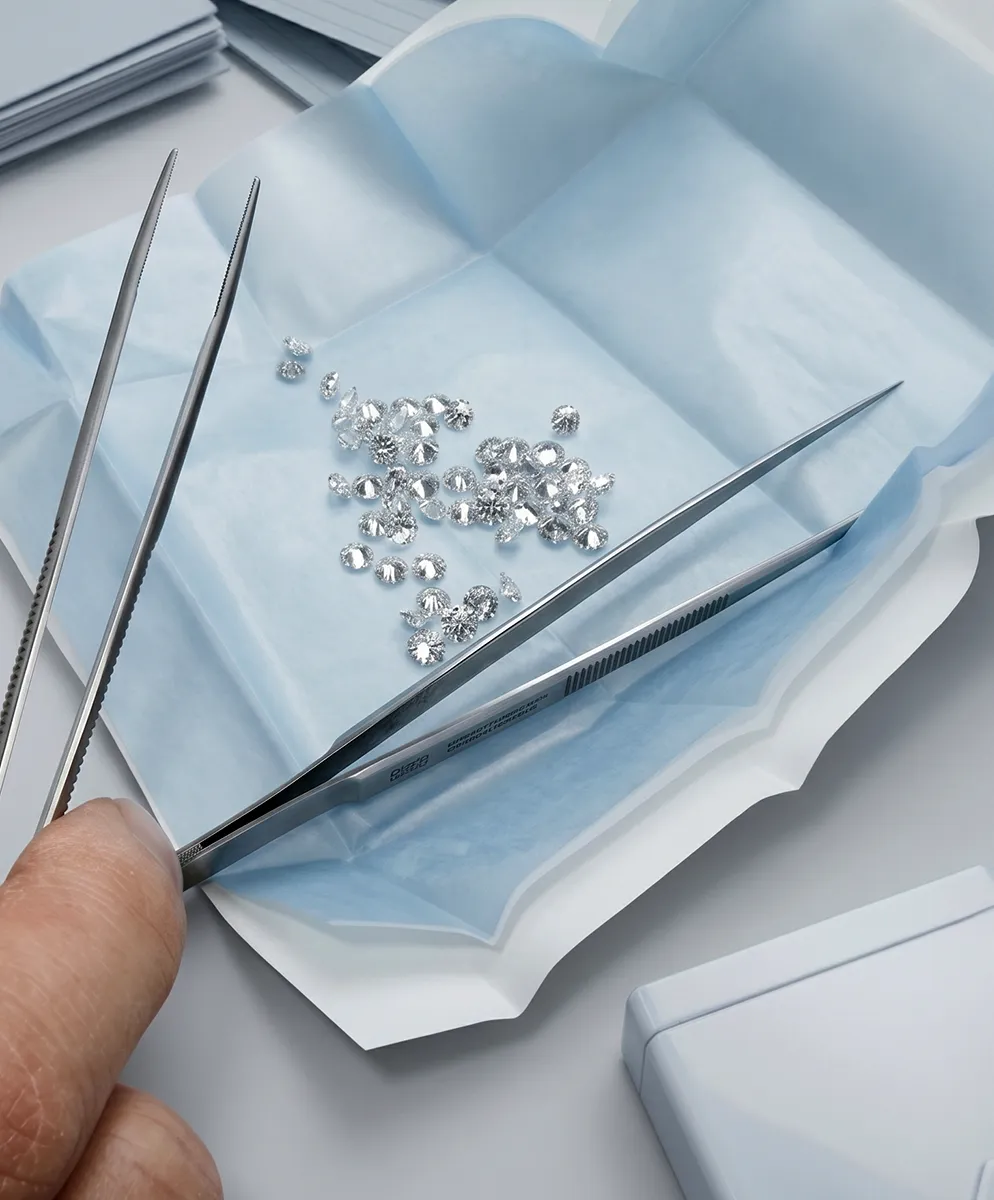 Person using tweezers to handle small diamonds on blue paper.