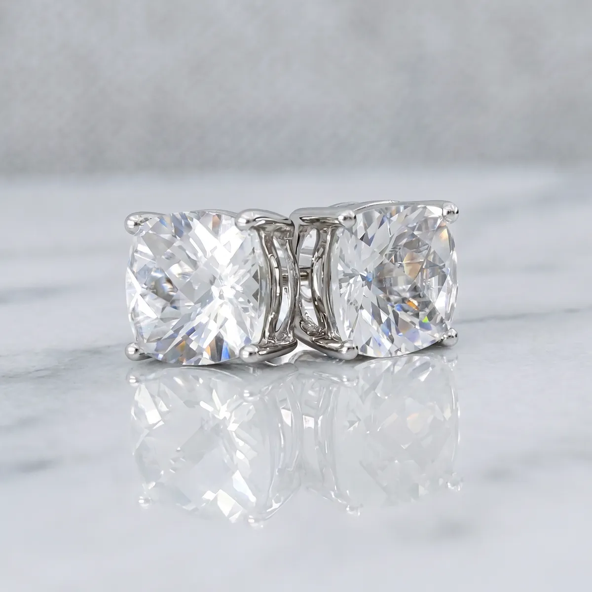 Diamond stud earrings with silver prongs on a marble surface.