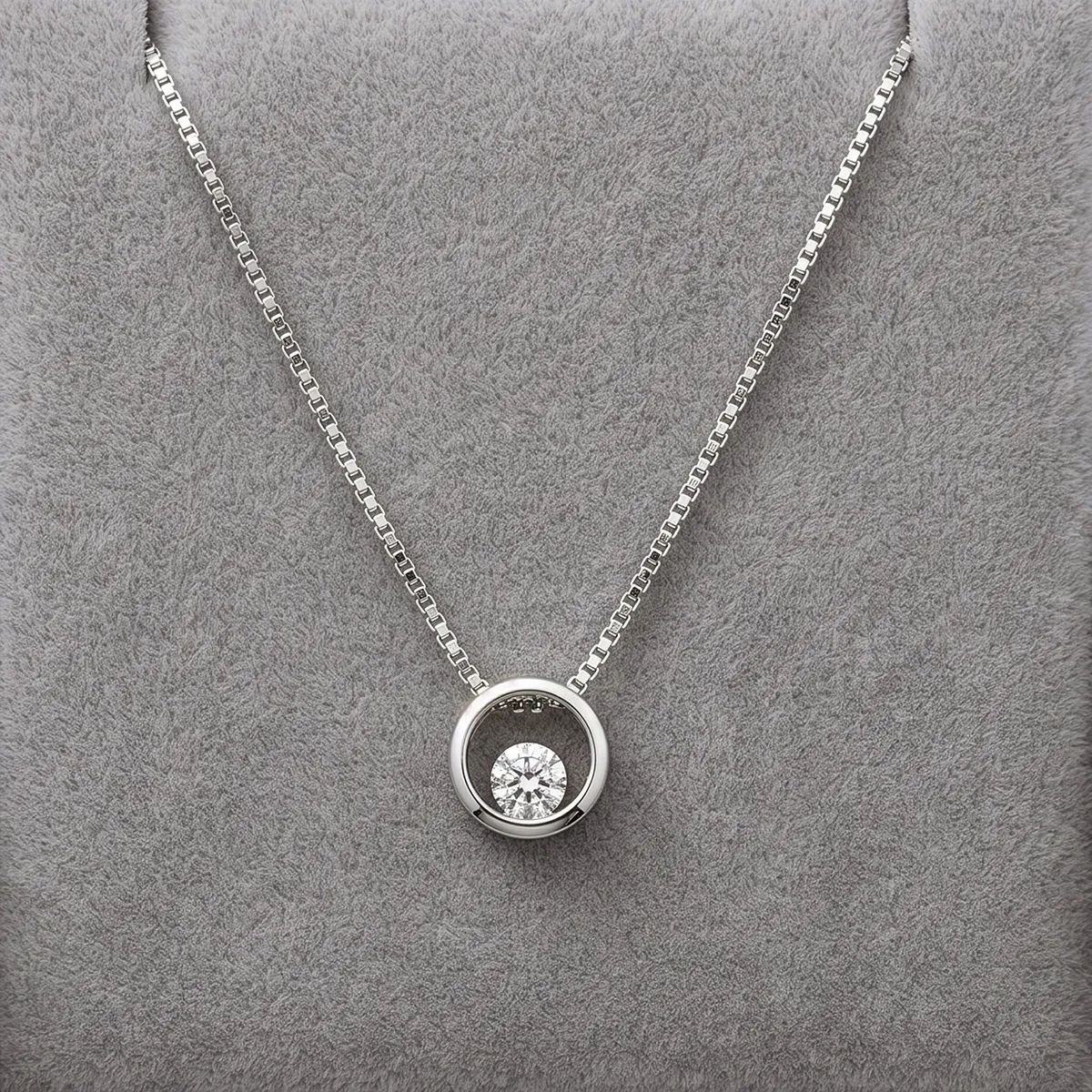 A silver necklace with a circular pendant featuring a diamond on a gray background.