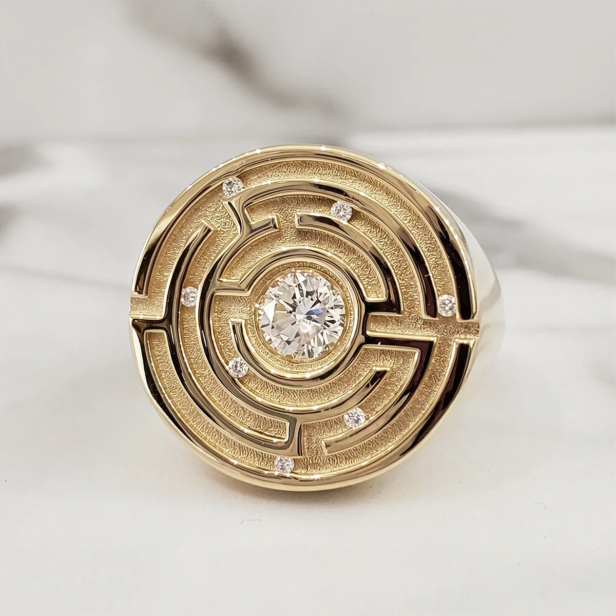 Gold ring with a maze design and central diamond on a marble surface.
